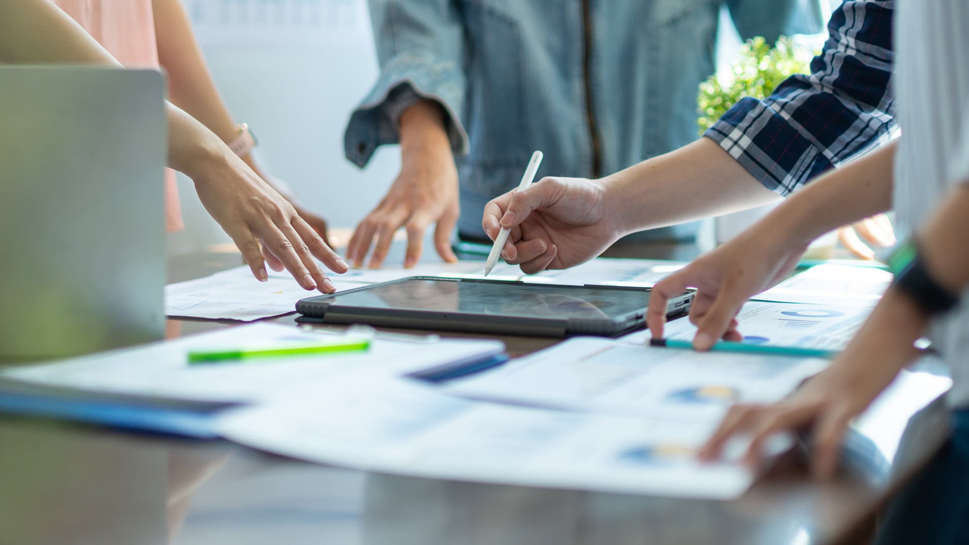 Equipo analizando informes con gráficos y usando una tableta con lápiz digital sobre una mesa