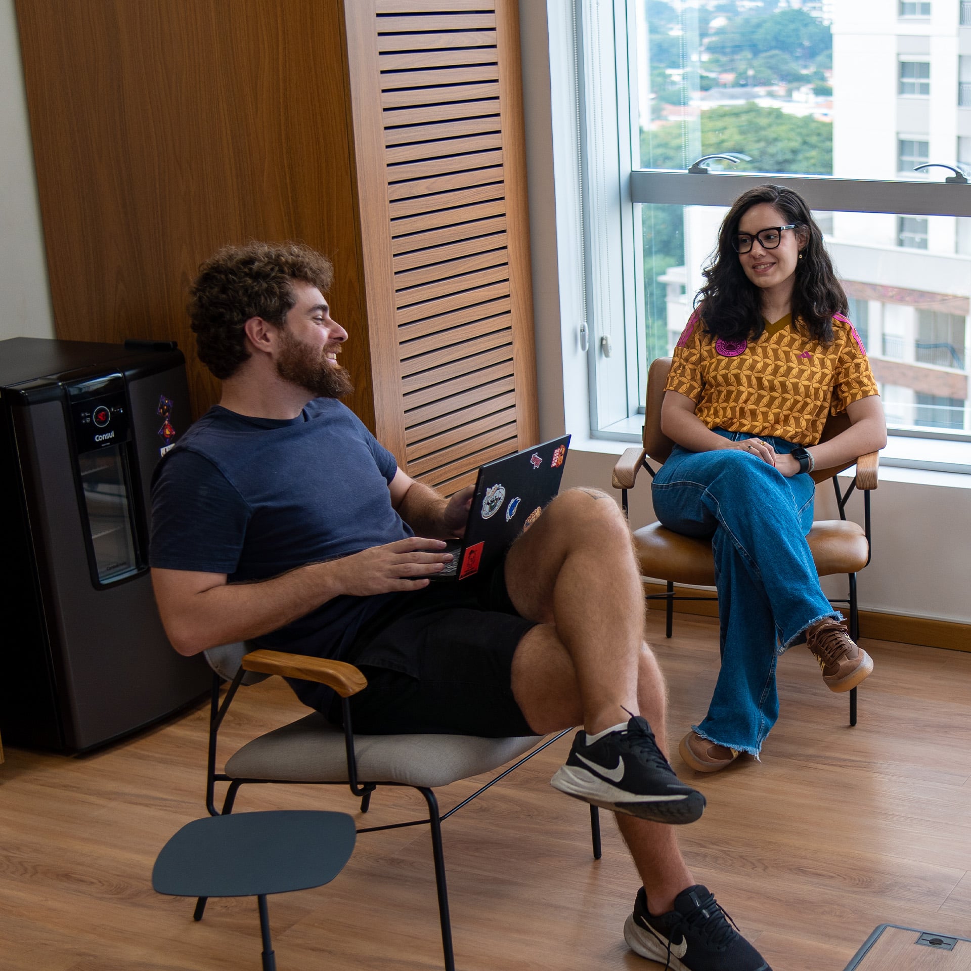 Duas pessoas a conversar na zona de descanso, uma com um portátil ao colo